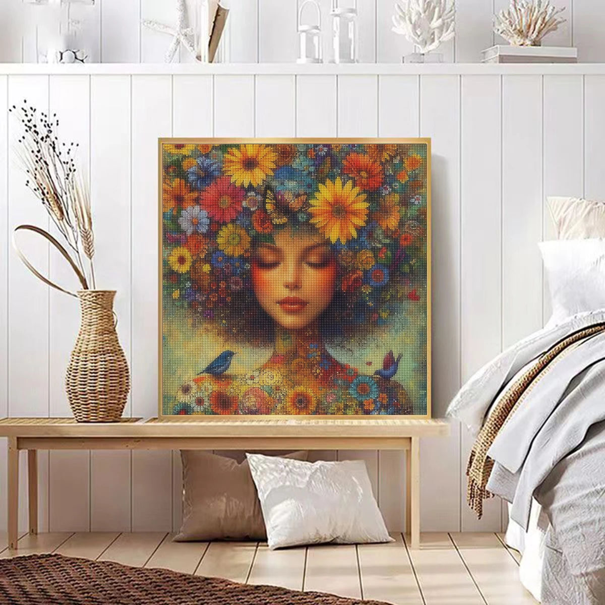 Diamond painting of a serene woman with closed eyes, her hair and body adorned with colorful flowers, butterflies, and birds. Place in a neutral wood frame decorating a minimalistic clean bedroom bringing a bright punch of colour to the space