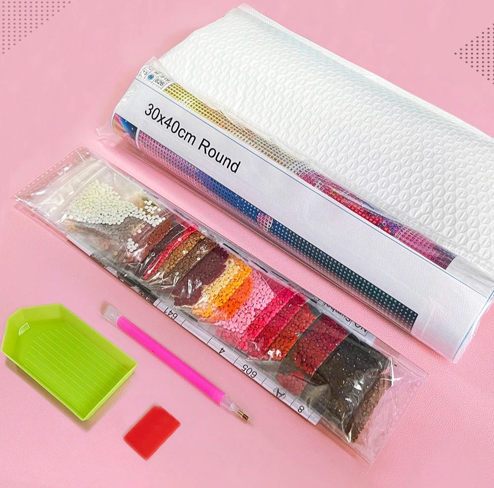 Packaging materials including diamond drills, diamond painting canvas, diamond drill applicator pen, glue and a tray on a pink background.