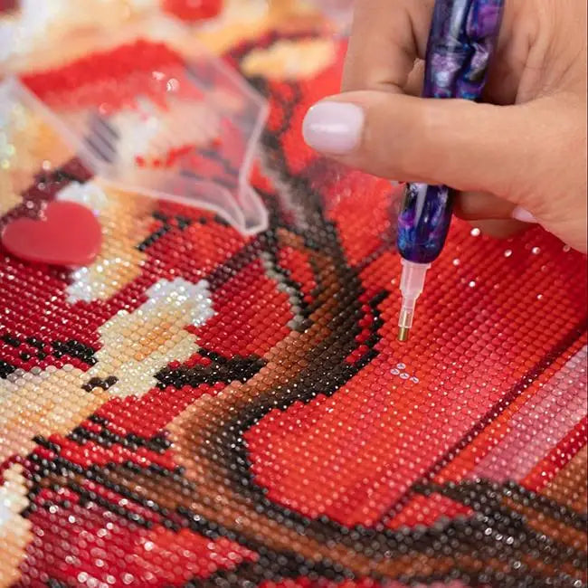 Hand using a diamond painting tool on a red and gold design